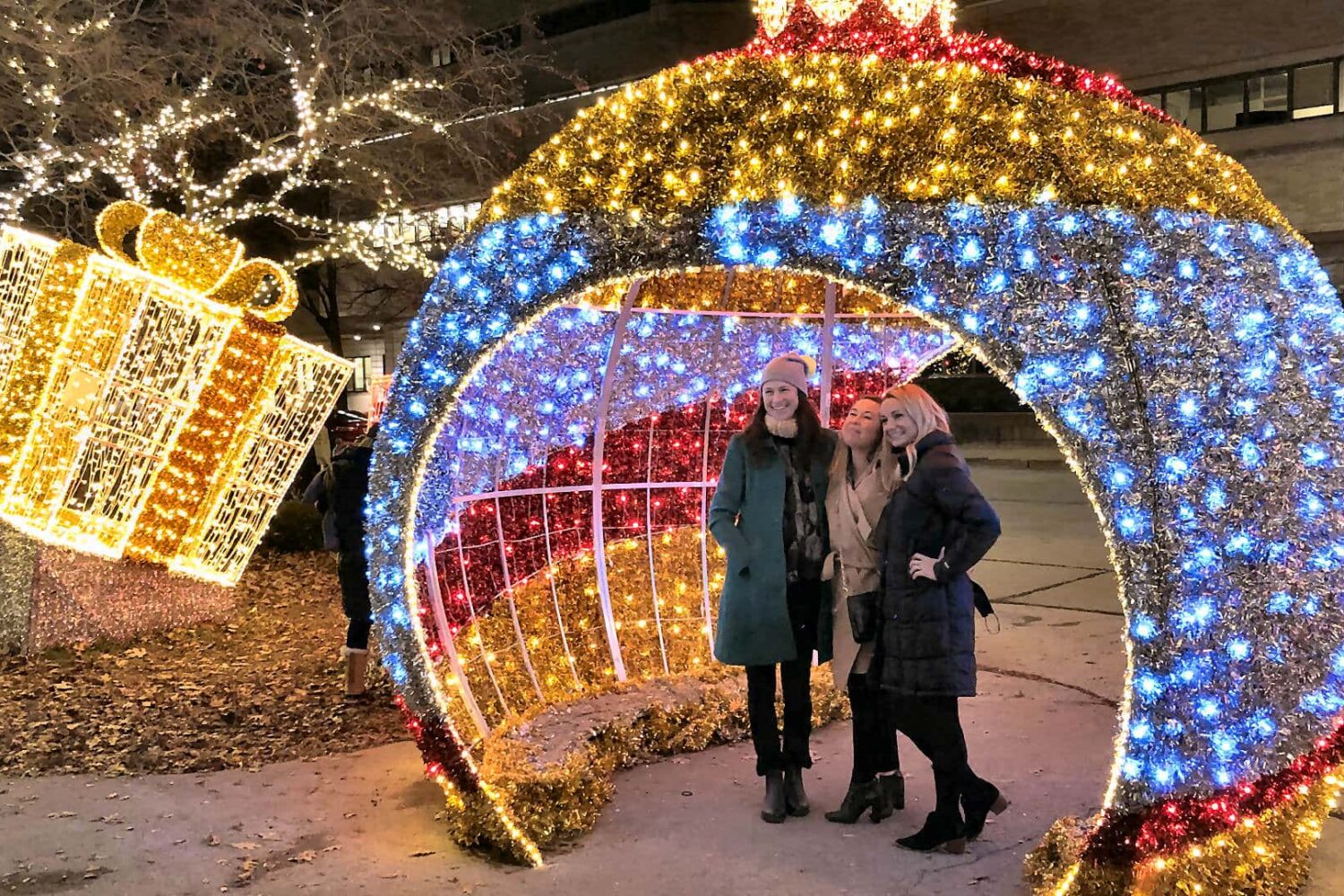 A group of 3 girls under a large lit Christmas ornament diagram