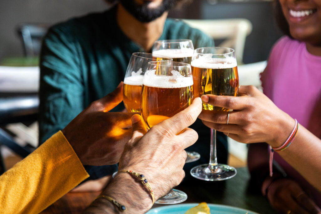 Close up of friends toasting with beer indoors. Friends having fun at bar cheering with beer. Celebrating. Friendship concept.