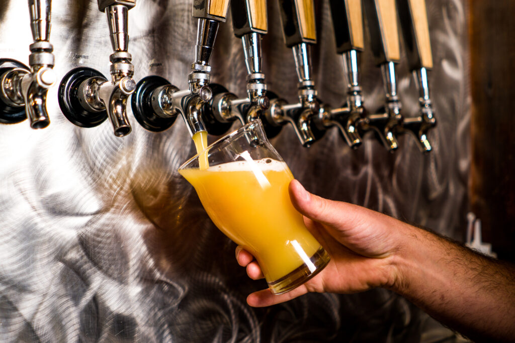A closeup of a Barman hand at beer tap pouring an Ice Cold IPA Craft Beer cup serving in a pub